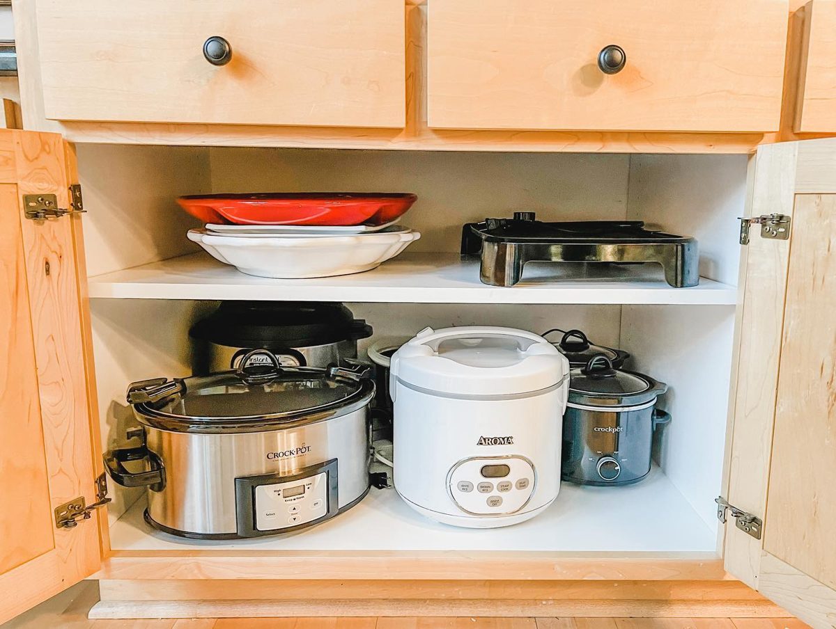 Cabinet with slow cookers, rice cooker, and serving dishes arranged for easy access